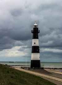 Lighthouse on beach against cloudy sky