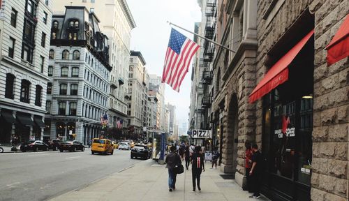 People on street amidst buildings against sky in city