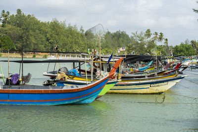 Boats moored on river by trees against sky