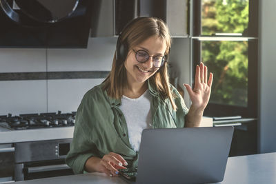 Young woman using phone while sitting on window