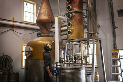 Side view of man looking at machinery at distillery