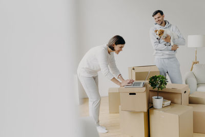 Smiling man looking at woman using laptop at new home