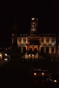 Illuminated building by street against sky at night