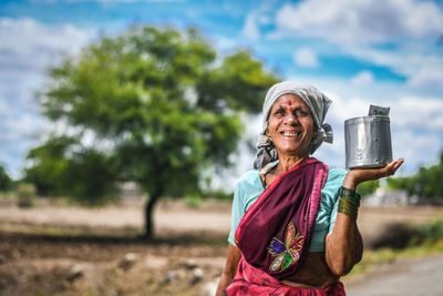 Portrait of smiling woman farmer holding container while standing outdoors