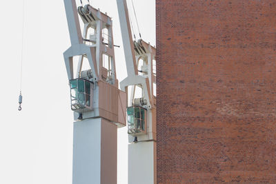 Low angle view of cranes by building against clear sky