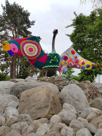 Multi colored rocks by trees against sky