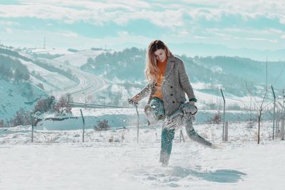 Young woman kicking snow on land during winter