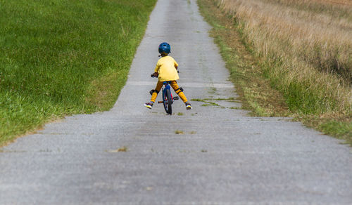 Rear view of man riding push scooter on road