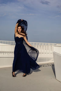 Portrait of young woman standing on railing against sky