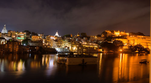 Illuminated city by sea against sky at night