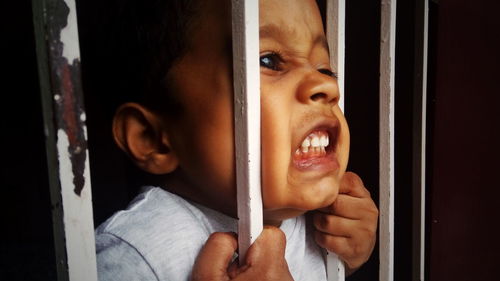 Close-up of aggressive boy holding security bars of window