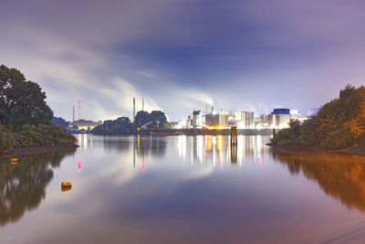 Illuminated buildings by river against sky in city