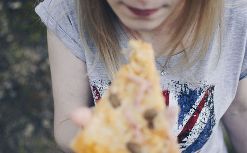 Midsection of young woman eating pizza while standing outdoors