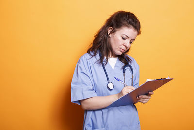 Young woman using mobile phone against yellow background