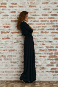 Full length of beautiful woman in black dress standing against brick wall