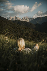 Woman lying on grass while looking at dolomites mountain ranges in south tyrol, italy