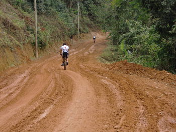 Rear view of man cycling on dirt road