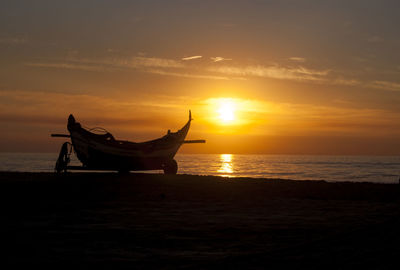 Silhouette boat on shore at beach against orange sky during sunset