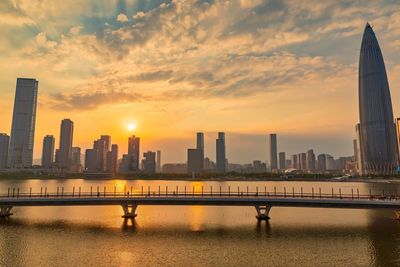 City by river against sky during sunset