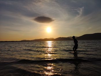 Silhouette boy wading in sea against sky during sunset