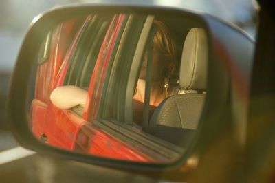 Reflection of woman sitting in car on side-view mirror