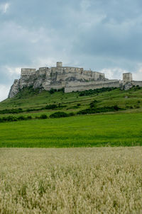 Low angle view of castle on field against cloudy sky