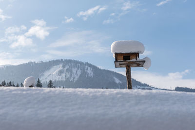 Homemade wooden bird's feeder in winter, under snow. mountain and cloudy sky at the background