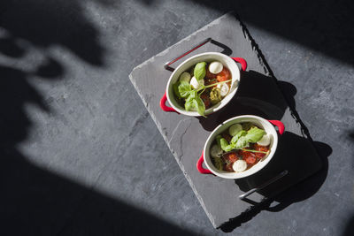 Baked cherry tomatoes in portioned saucepans in the sunlight on the table, flat lay, copy space