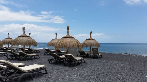 Chairs on beach by sea against sky