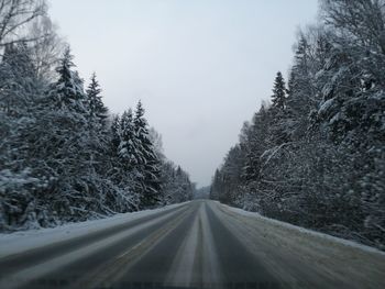 Road amidst snow covered trees against sky