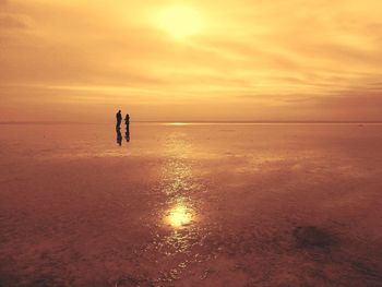 Silhouette people on beach against sky during sunset