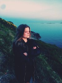 Beautiful young woman standing by sea against sky