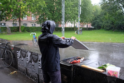 Rear view of man wearing hooded shirt preparing barbeque at yard