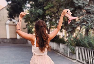 Rear view of woman with arms raised standing against trees