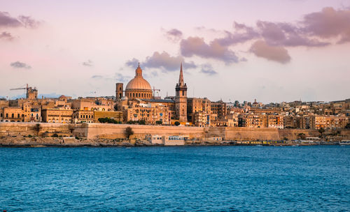 Buildings at waterfront against cloudy sky