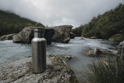 Water flowing through rocks by river against sky