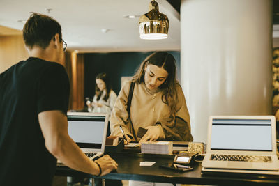 Man looking at woman signing at reception desk in hotel lobby