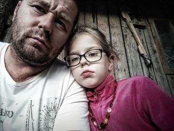 Low angle portrait of father and daughter sitting by closed wooden door