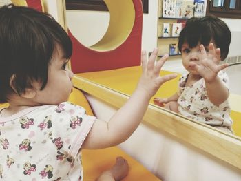 Cute baby girl touching mirror at home