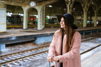 Young woman with suitcase on platform of station. traveler girl waiting