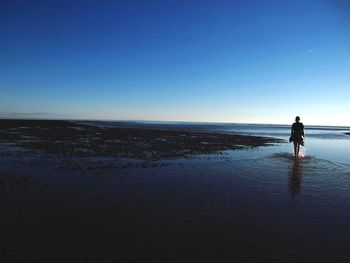 Rear view of woman walking in sea against clear blue sky