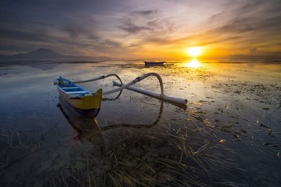 Boat moored on beach against sky during sunset