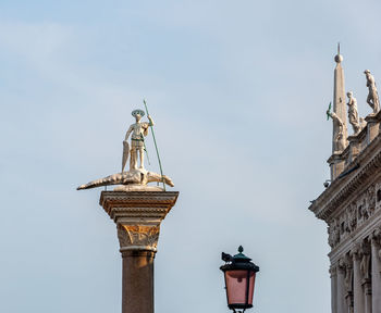 Low angle view of statue by street light against sky