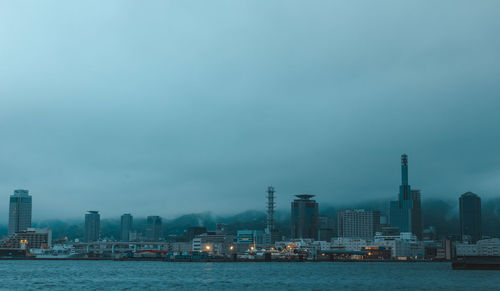 Buildings by river against cloudy sky at dusk