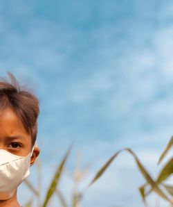 Boy wearing mask looking away against sky