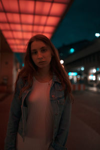 Portrait of woman standing on footpath under illuminated lights