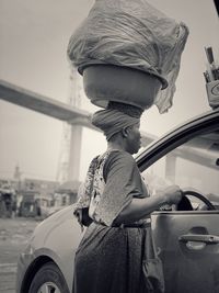 Woman carrying tub on head while standing by car