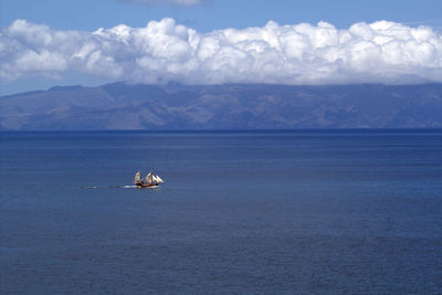 Boat sailing on sea against mountains and cloudy sky