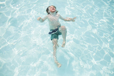 Young boy swims on back submerged in pool with face in the sun