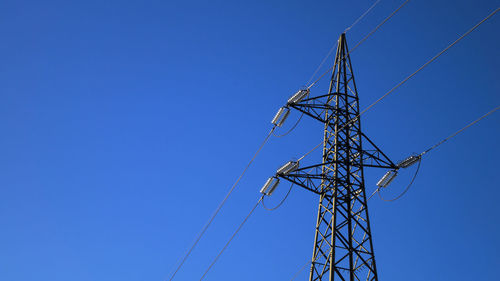 Low angle view of electricity pylon against clear blue sky